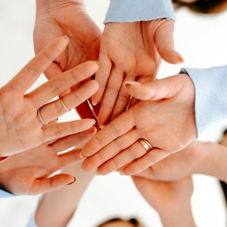 Mehrere Hände, die sich aufregend in der Mitte treffen, verschiedene Ringe sichtbar.