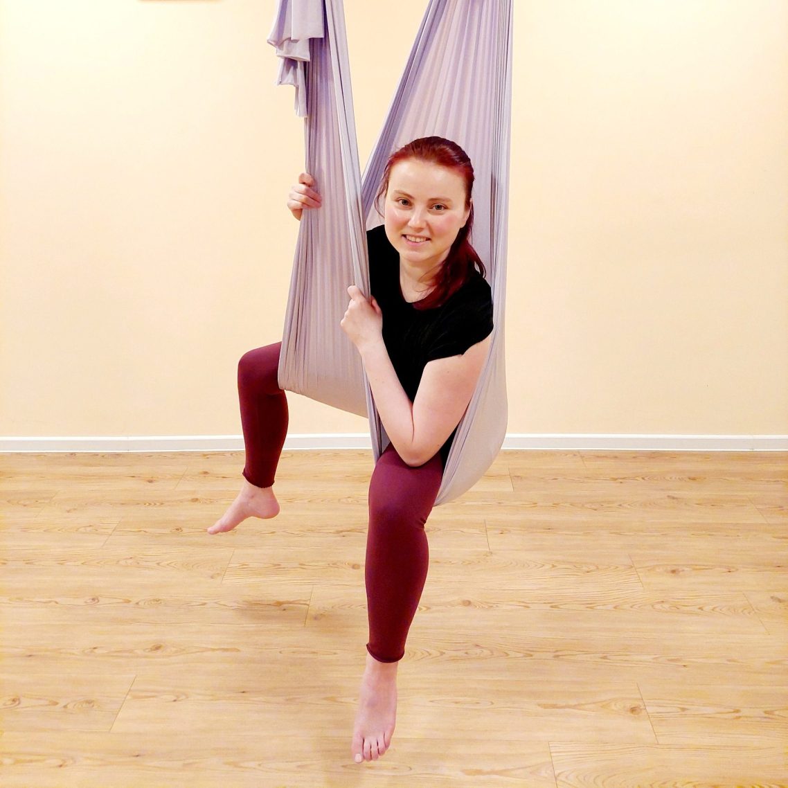 Frau hängt in einem Tuch, lächelt und posiert in einem Trainingsraum.