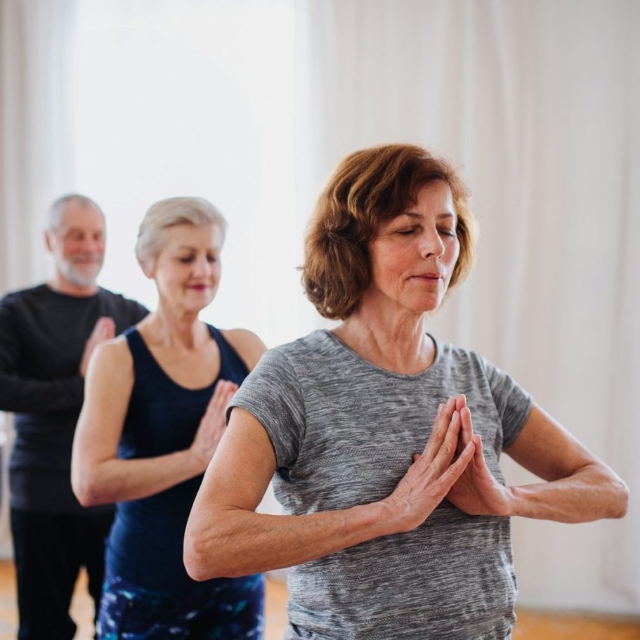 Ältere Menschen praktizieren Yoga in einem hellen Raum, einige meditierend, andere aufmerksam.