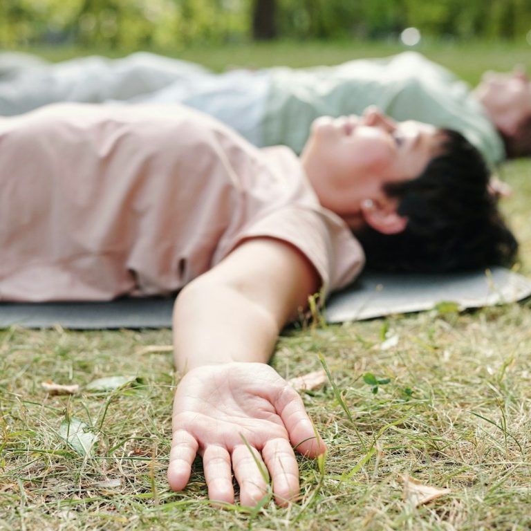 Zwei Personen liegen auf dem Boden in entspannter Haltung, mit ausgestreckten Armen.