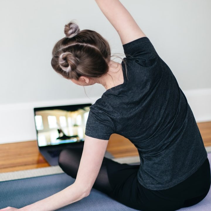 Eine Person macht Yoga-Übungen vor einem Laptop in einem hellen Raum.