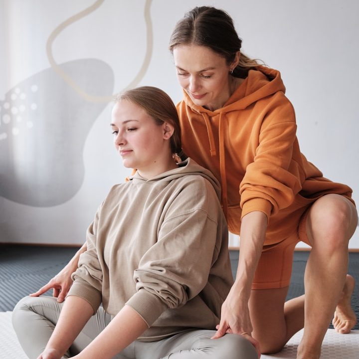 Zwei Frauen in bequemer Kleidung üben eine Yoga- oder Entspannungsübung.