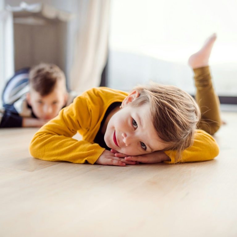 Zwei Kinder liegen auf dem Boden, eines lächelt und das andere schaut im Hintergrund beim pilates